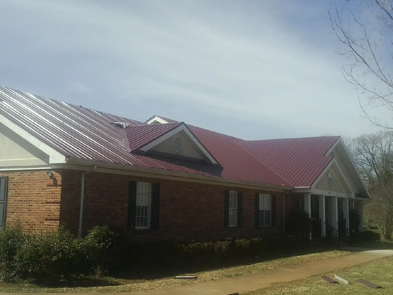Red metal roof with gabled entries on a long brick building, from a Hail Damage Roof Repair job in Drexel