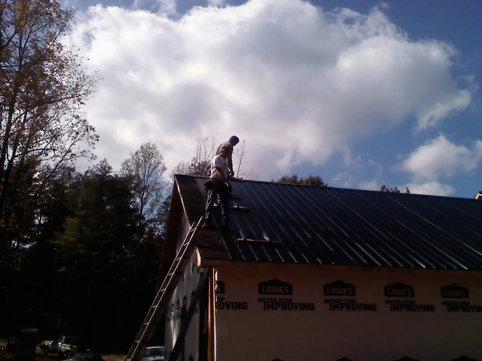 Roofer fastening dark metal panels high against a cloudy sky, from a Roof Inspection job in Drexel