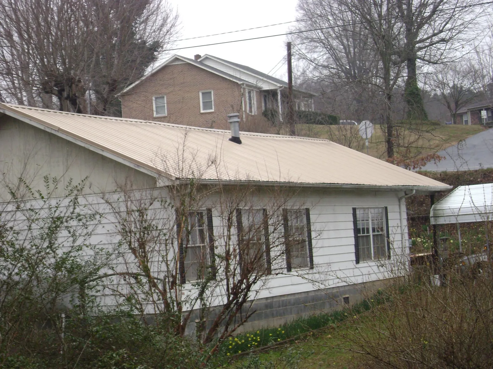 Tan metal roof on a white sided house set into a hillside — Commercial Roofing by Roofing Brothers in Drexel
